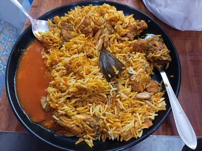 A Meitei festive rice dish with a rich red sauce on a black plate