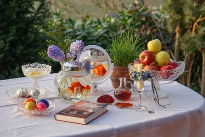 A table with goldfish in a bowl, apples, sprouts, flowers and a book