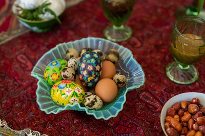 A glass dish of painted eggs on a red Persian carpet