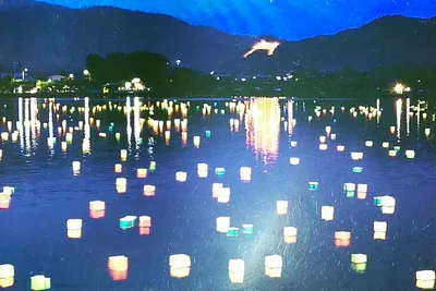 Many paper lanterns float on a dark lake below a hillside fire
