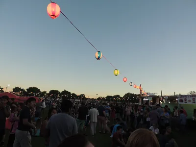Strings of round paper lanterns over a large crowd at dusk