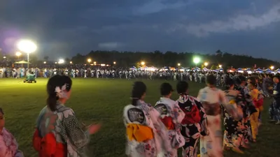 Women in bright yukata dance on a field at night under lights