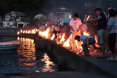 Small fires burn in a row along a river wall at night