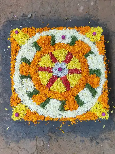 Square Onam pookalam of orange, white and yellow flowers with a wheel in the middle
