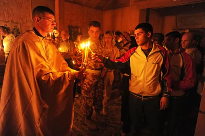 Worshippers hold candles lit from the priest's flame in a dark church