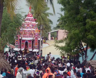 A tall decorated temple car pulled through a large crowd under trees