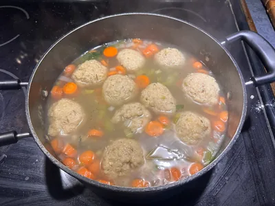 A pot of matzah ball soup with carrots and herbs