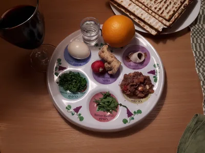 A Seder plate with egg, bitter herbs, greens and an orange beside matzah