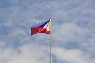 The flag of the Philippines flying against a cloudy blue sky