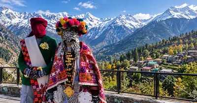 A Kinnauri village deity decked with bright flowers and shawls, with snow peaks behind