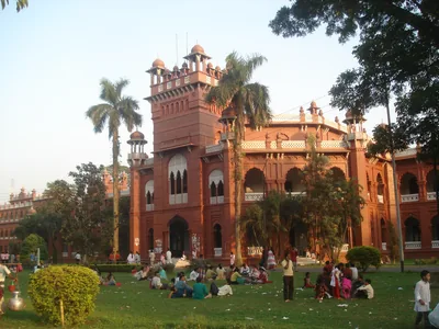 A red brick building with towers and arches behind a lawn where groups of people sit together