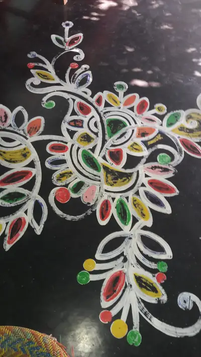 A painted alpana design of white swirls and colourful leaves on a black ground