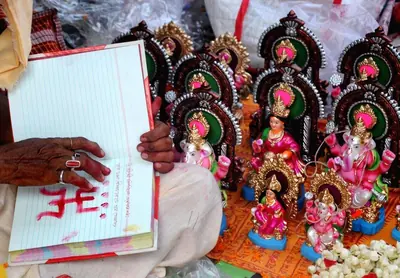 A priest holding a red account book beside small clay images of deities