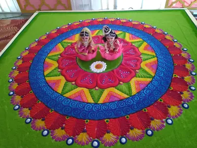 A large round kolam in bright pink, blue, yellow and green with two decorated pots at its centre