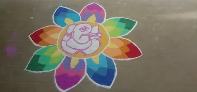 A colourful rangoli of rainbow petals around a white drawing of Ganesha