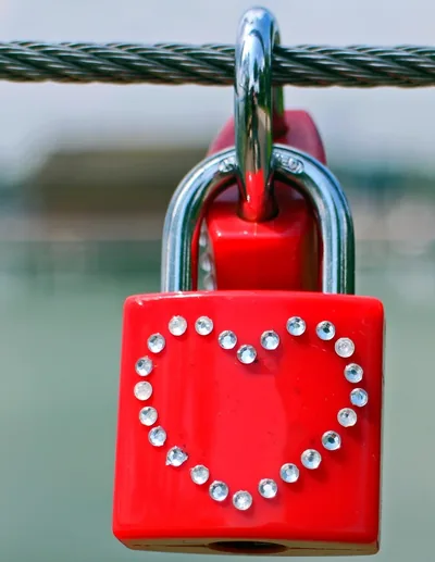 A red padlock with a sparkling heart hanging on a bridge