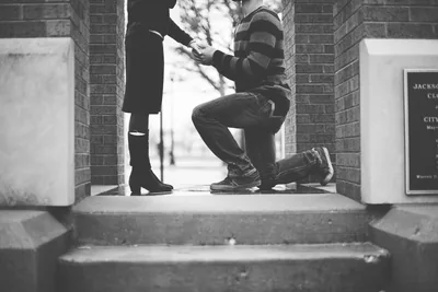 A man kneeling to hold a woman's hand in a doorway