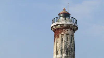 An old white and red lighthouse tower against a blue sky