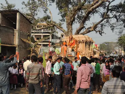 People gather under a big tree around a tall carved chariot