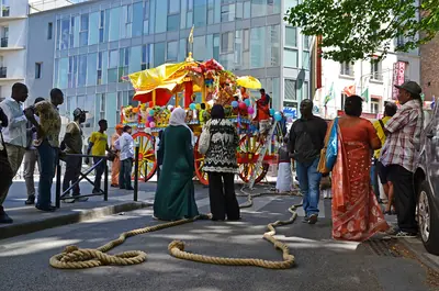 A colourful chariot stands on a city street with long ropes laid in front