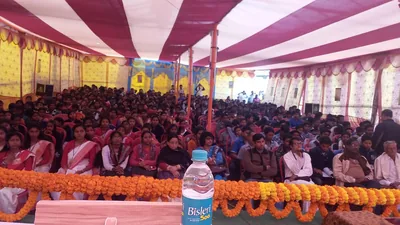 A large crowd seated under a striped tent with marigold garlands in front