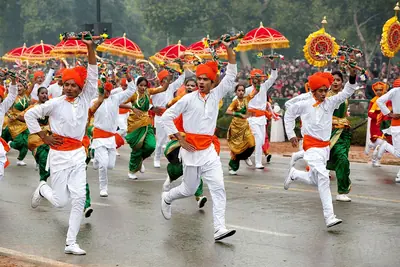 Young folk dancers in white with orange turbans and sashes, and women in green saris, dancing down the parade avenue