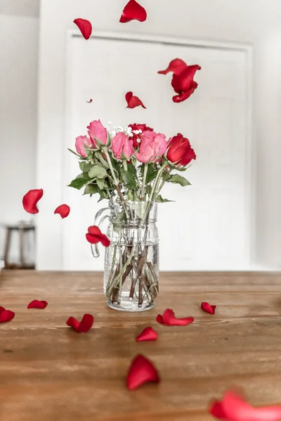 Pink roses in a glass jar with petals on the table