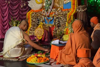 A priest offers flowers before a decorated altar of the goddess with plates of fruit