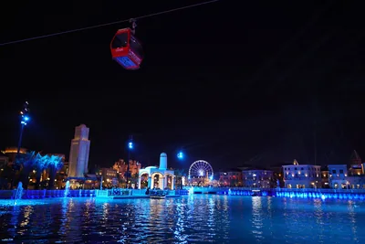A lit waterfront with a big wheel and cable cars at night