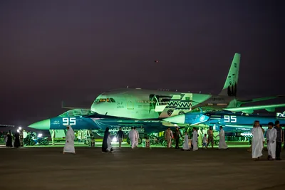 A jet lit in green light on display as families walk around it at night