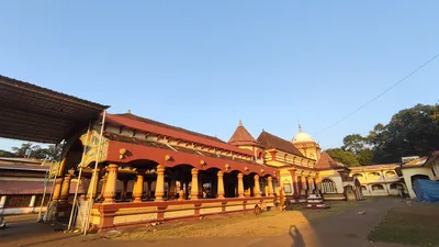 A red and gold Goan village temple with long pillared halls under a blue sky