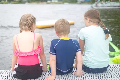 Three children sitting by a lake, seen from behind