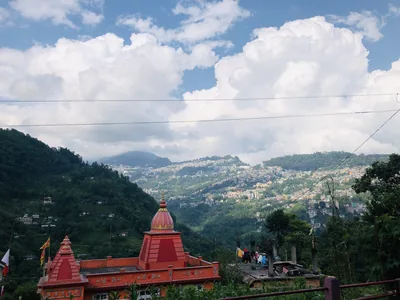 A red temple roof with green hills and white clouds behind