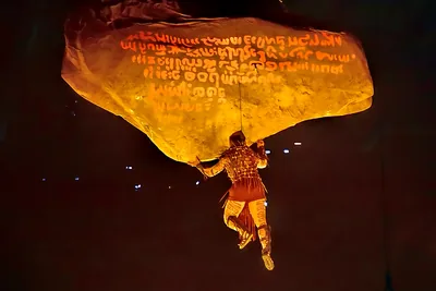 A performer hangs beneath a giant glowing stone in a night show