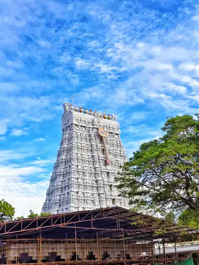 A tall white temple tower beside green trees under a bright blue sky