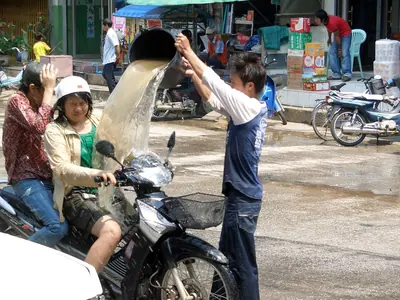 A man pouring a bucket of water on a passing motorbike rider in a street