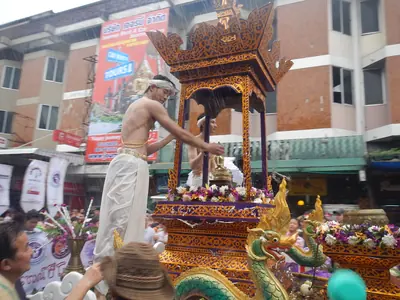A man pouring water over a Buddha image on a gilded float