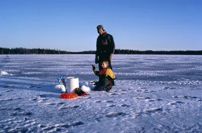 A father and son getting ready for ice fishing on a frozen lake under blue sky
