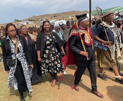 A crowd in traditional dress, beadwork and headwear walks across an open field