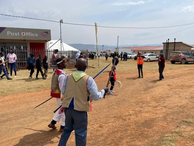 People in traditional dress gather on a dusty field with flags and tents