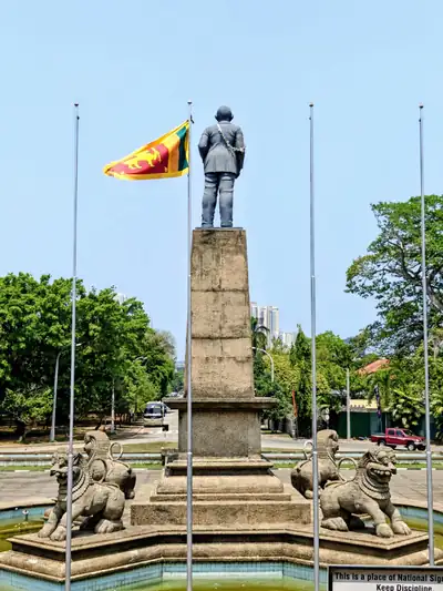 A statue on a tall pillar with the Sri Lankan lion flag flying beside it