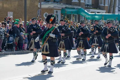 A pipe band in kilts marching down a street lined with spectators