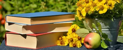 A stack of books with sunflowers and a red apple in a garden