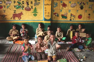 Children sitting on a mat in a brightly painted classroom with letters and pictures on the walls