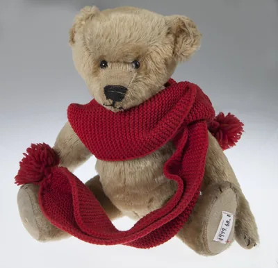 An old teddy bear wearing a red knitted scarf