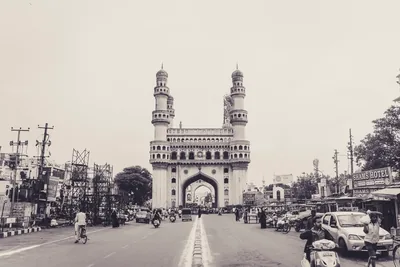 Black and white photo of the Charminar over a wide road with traffic