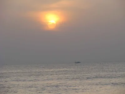The sun rising over a calm sea with a small boat