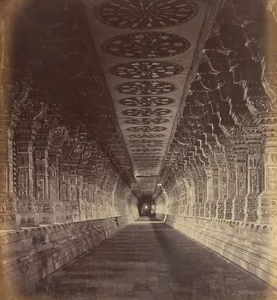 Old photo of a long temple corridor lined with carved pillars