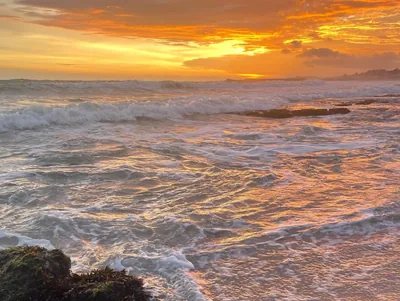 Waves breaking on rocks under a golden sunrise sky