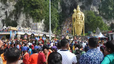 A huge crowd of pilgrims below a giant golden statue of Murugan and steps up a limestone hill